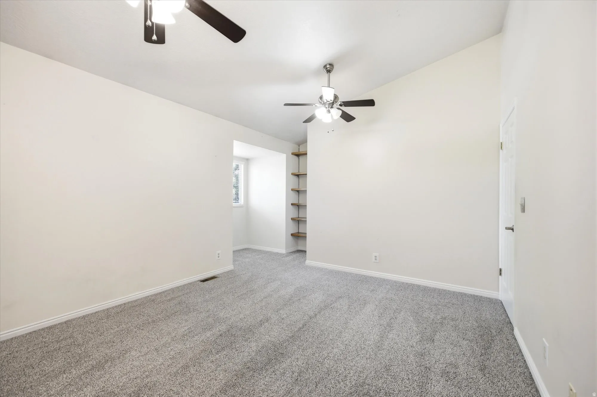 Spacious room featuring vaulted ceilings, light gray carpeting, and two ceiling fans