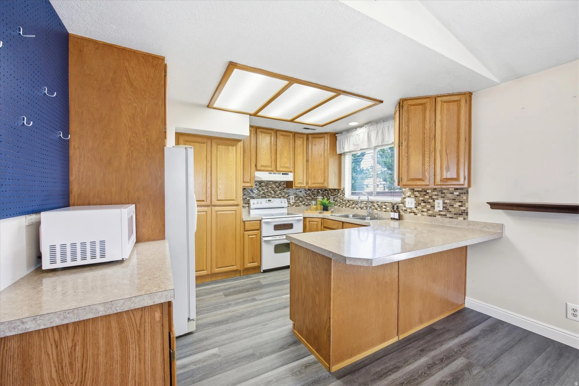 Kitchen featuring wood-finish cabinetry, light-toned countertops, a mosaic tile backsplash, wood-finish flooring, and an integrated ceiling light fixture
