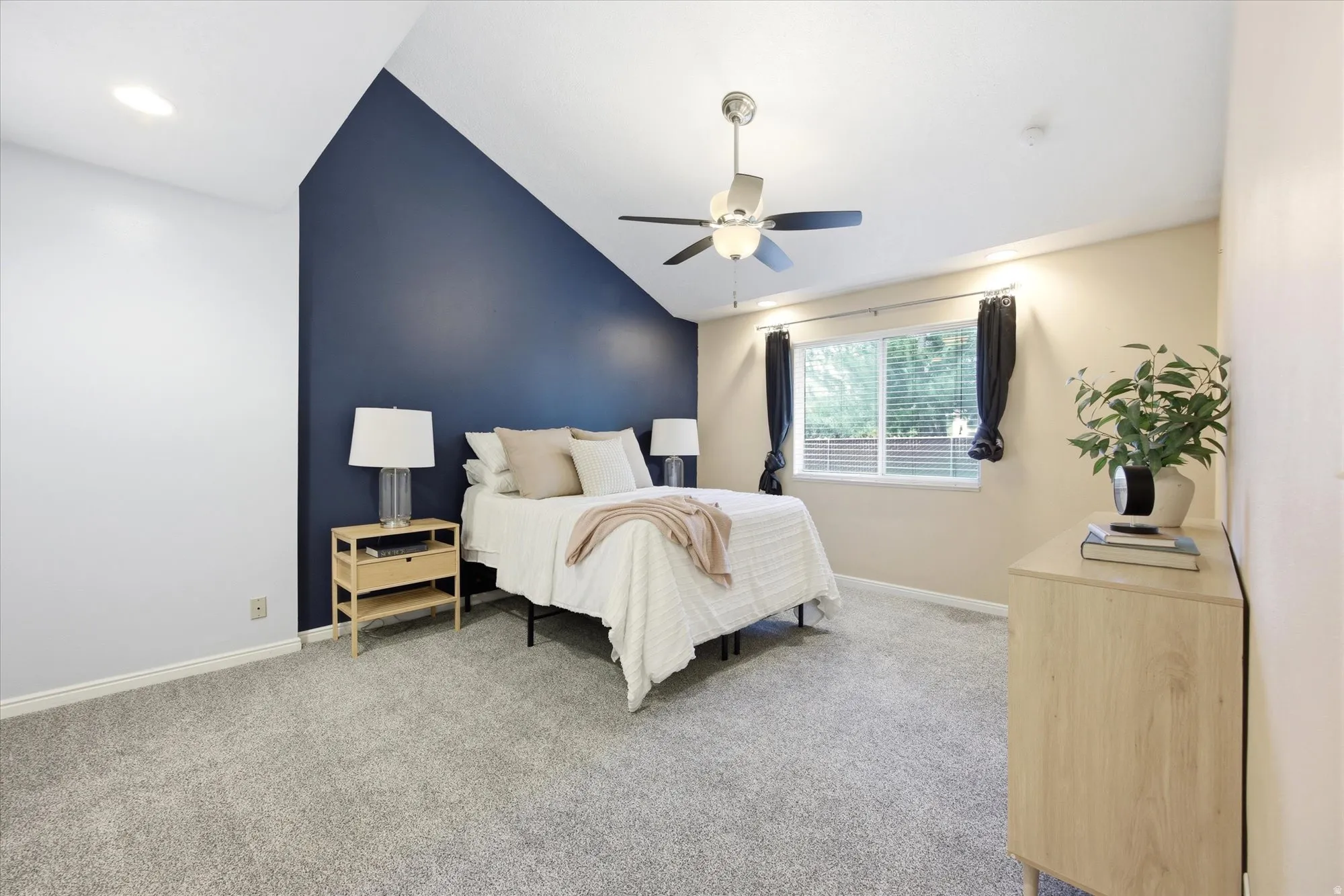 Vaulted ceiling bedroom featuring a ceiling fan with integrated lighting, a large window with white blinds, and plush carpeting