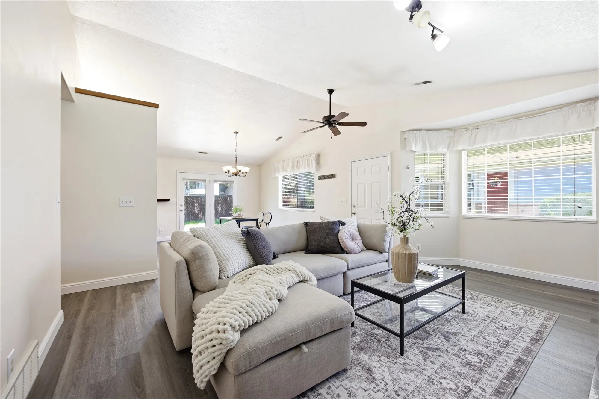 Vaulted ceiling living area featuring wood-finish flooring, a ceiling fan, and large windows with blinds