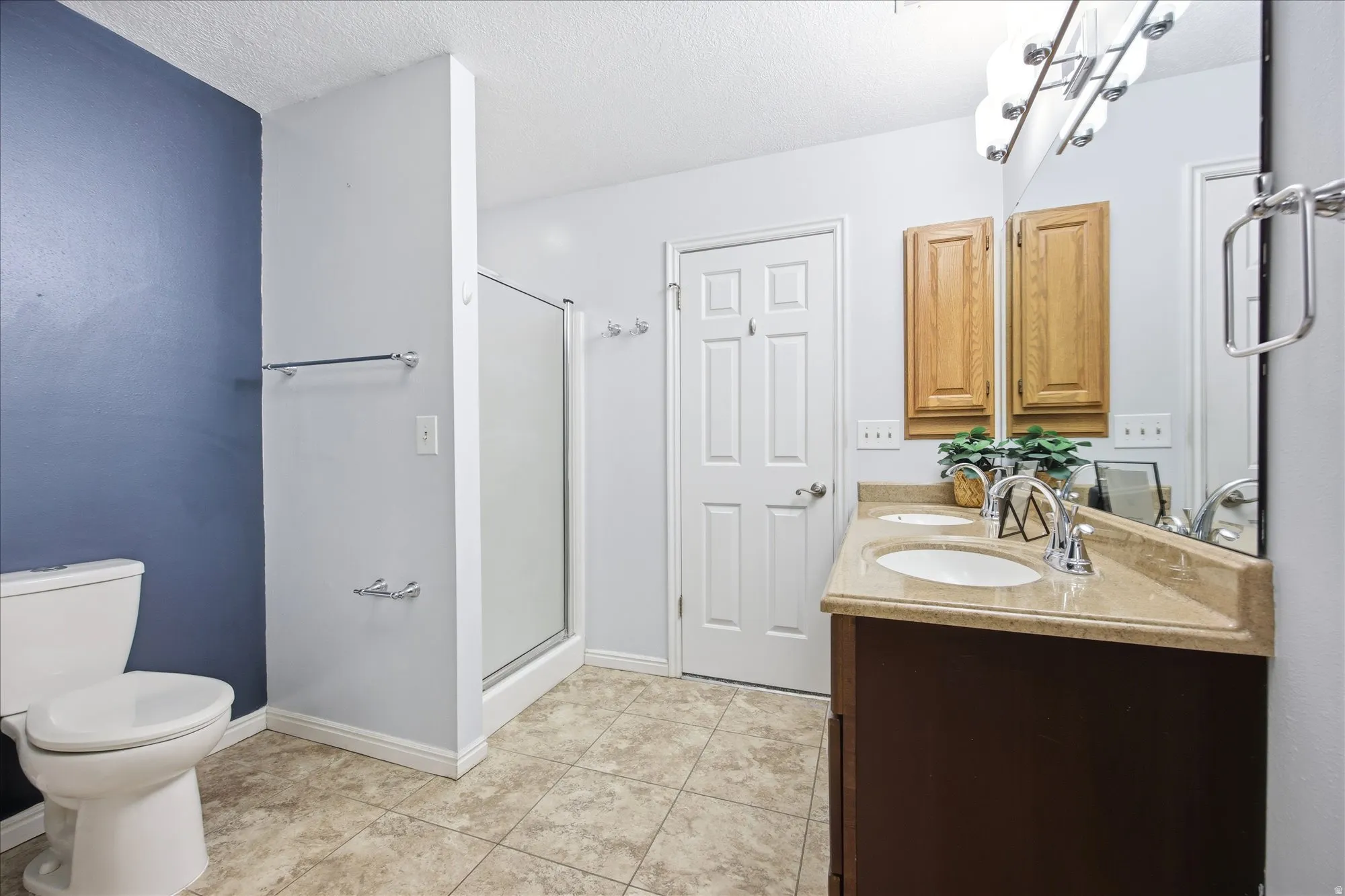 Bathroom featuring a dual-sink vanity with a stone-finish countertop, a stand-up shower with frosted glass enclosure, and tile flooring