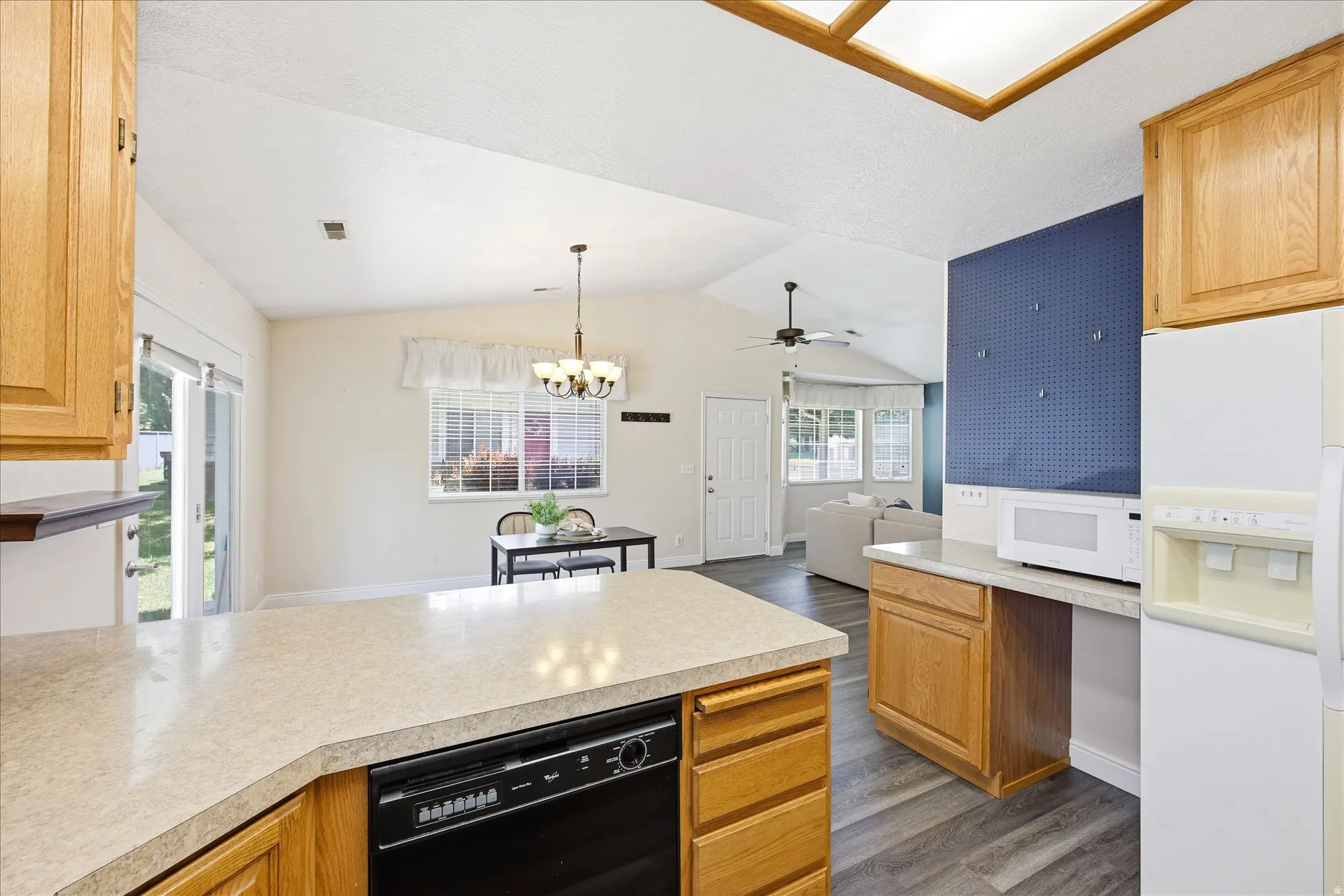 Open-concept living space featuring a kitchen with a peninsula island and wood cabinetry, a dining area with a chandelier, and a living area with a vaulted ceiling and bay windows