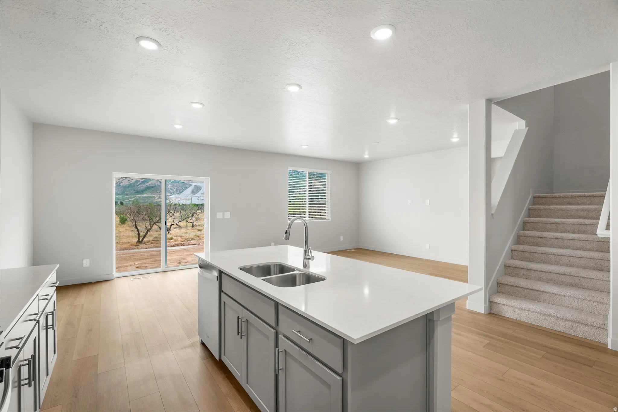Open-concept kitchen and living area featuring wood-finish flooring, recessed lighting, and a kitchen island with a double stainless steel sink
