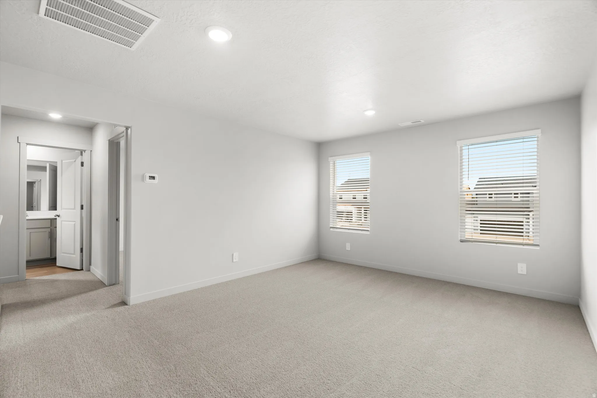 Carpeted room with recessed lighting and two windows featuring blinds