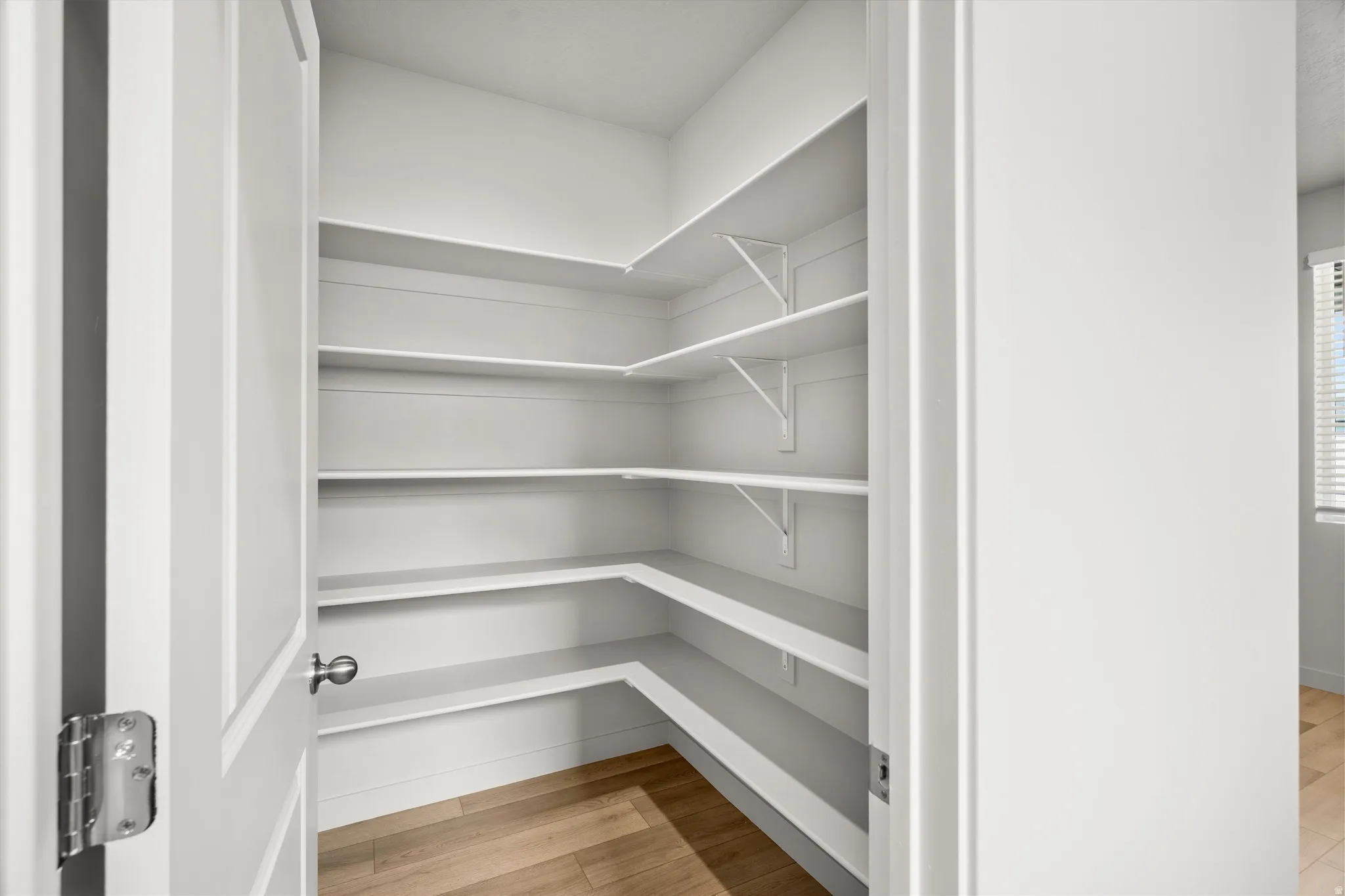 Corner pantry featuring multiple white built-in shelves and light wood-finish flooring