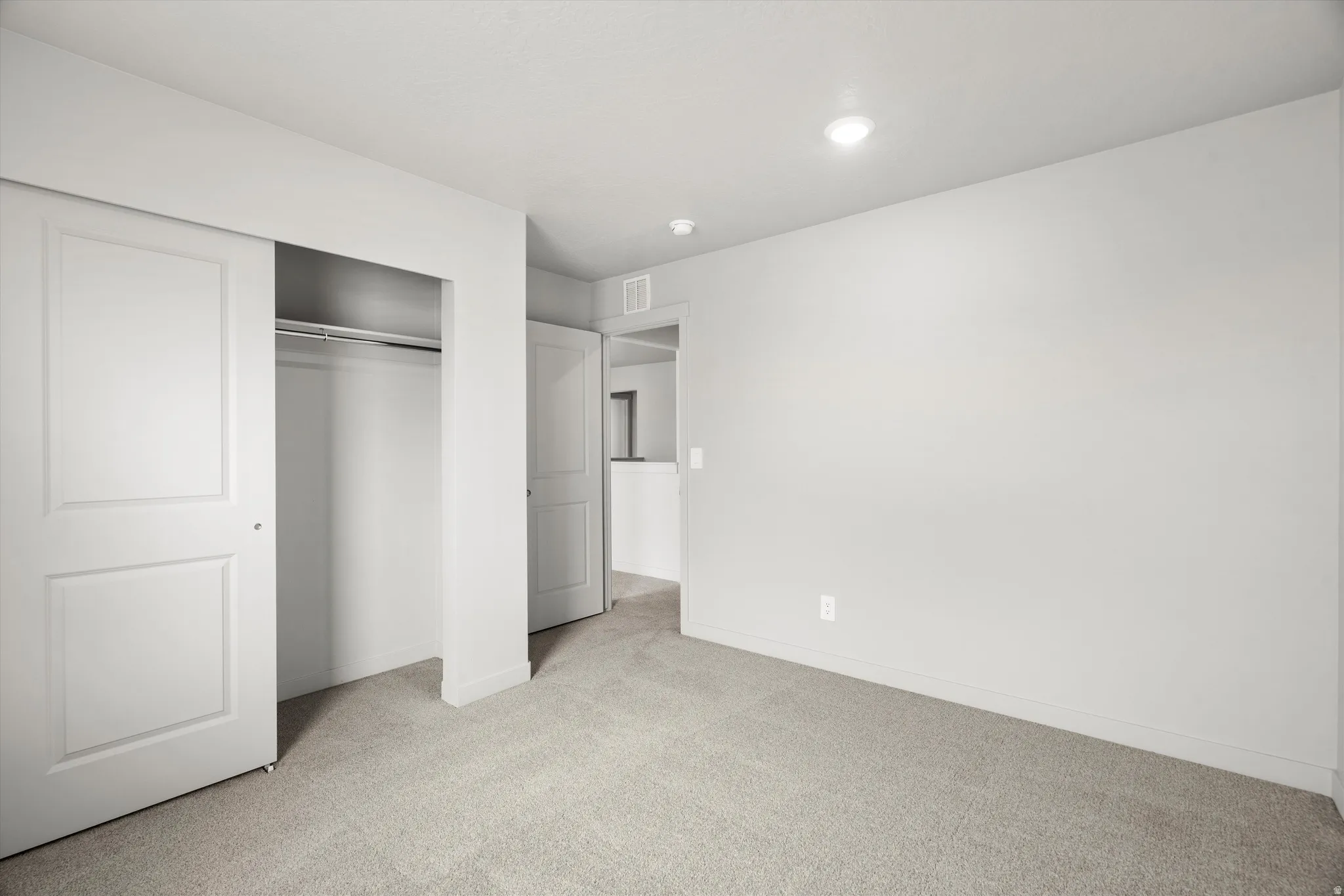 Carpeted room featuring recessed lighting, a sliding door closet with a metal hanging rod, and light-toned walls