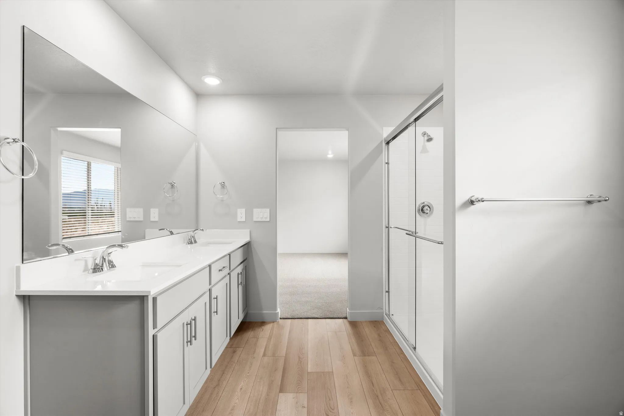 Bathroom featuring a double vanity with white countertops, light wood-finish flooring, a glass-enclosed shower, and a large mirror