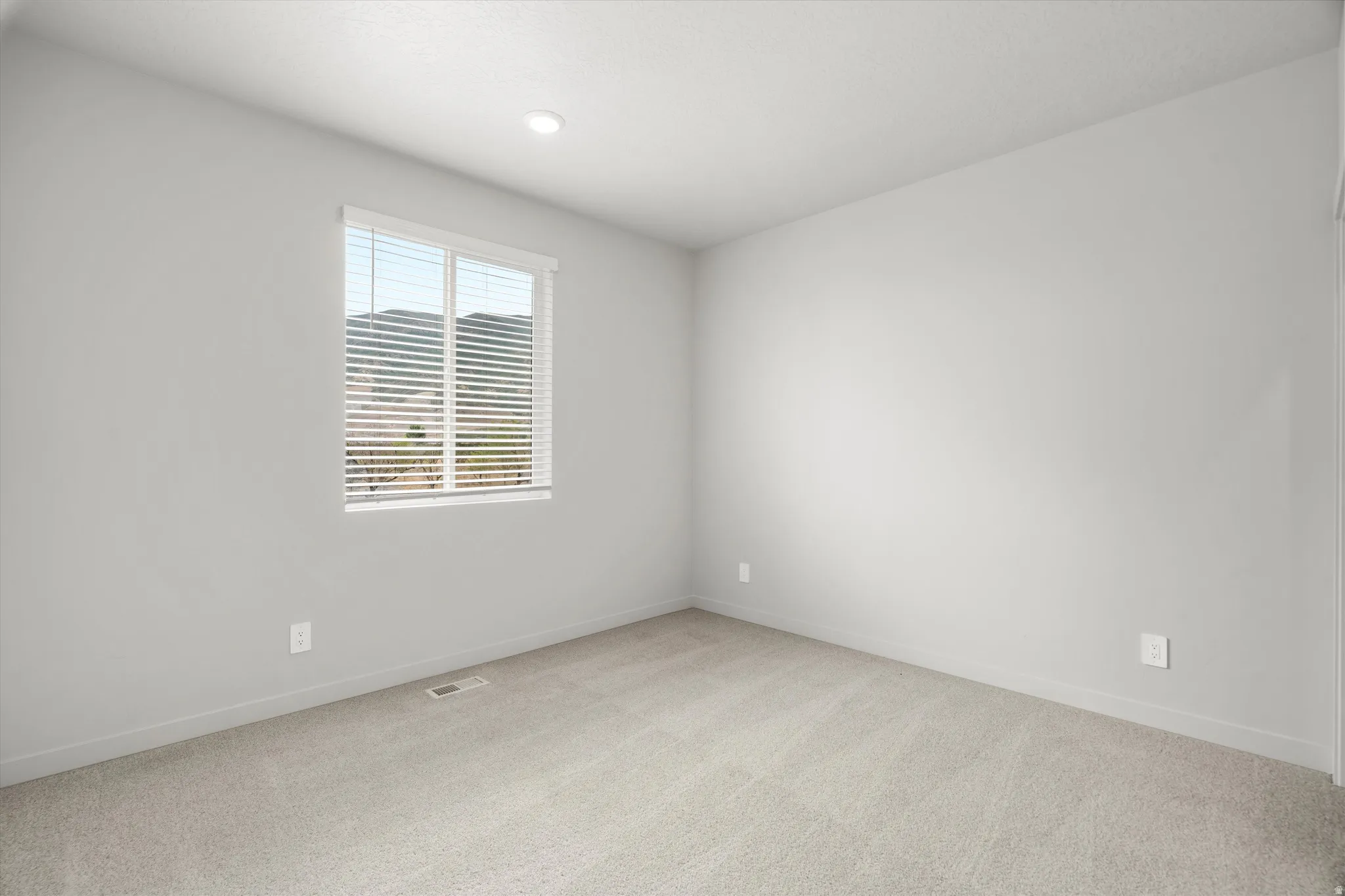Neutral-toned room featuring a large window with horizontal blinds, carpeted flooring, and recessed ceiling lighting