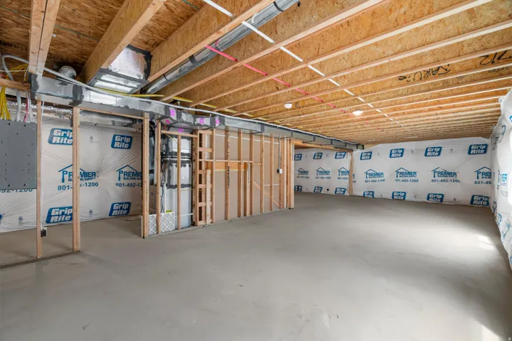 Unfinished basement featuring exposed wood joists and subflooring, concrete flooring, and insulated walls