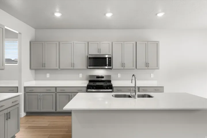 Modern kitchen featuring light gray cabinetry, white countertops, stainless steel appliances, and a central island with a double basin sink