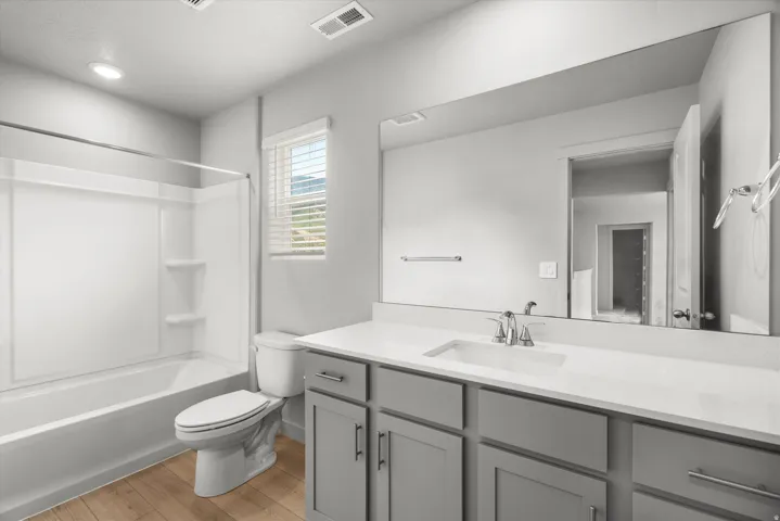 Bathroom featuring light gray walls, wood-finish flooring, and a white tub/shower combination