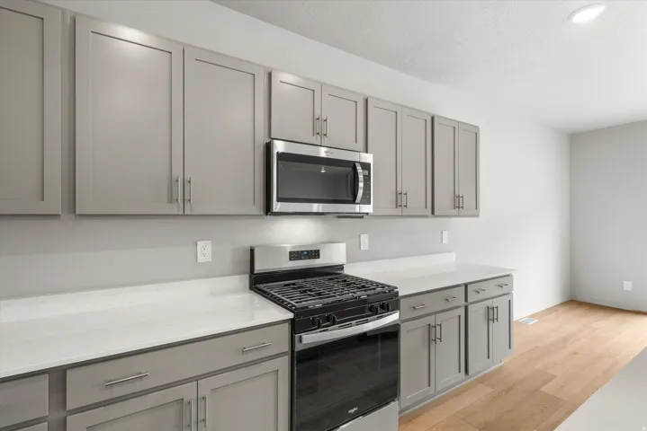 Kitchen featuring light gray cabinetry, stainless steel microwave, stainless steel range, light countertops, and wood-finish flooring