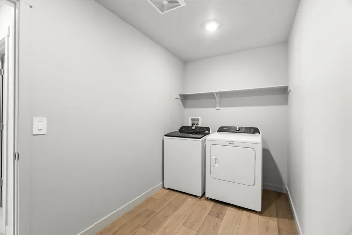 Dedicated laundry area featuring wood-finish flooring, a wall-mounted shelving unit, and a ceiling light fixture