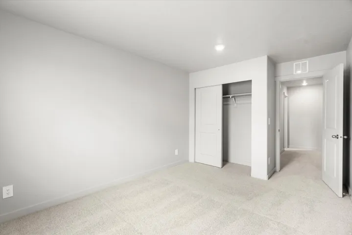 Carpeted room with light gray walls, featuring a bi-fold closet with a hanging rod