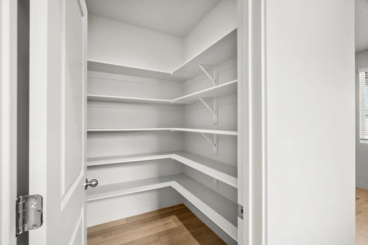Corner pantry featuring multiple white built-in shelves and light wood-finish flooring
