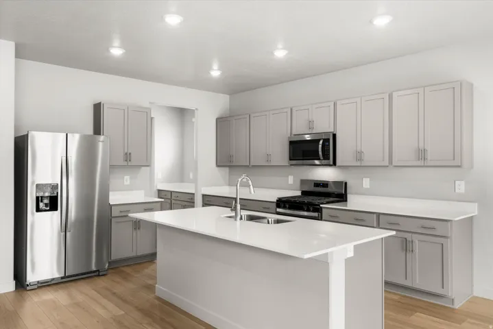Contemporary kitchen featuring an oversized island with an integrated sink, stainless steel appliances, light wood-finish flooring, recessed lighting, and gray shaker-style cabinetry with coordinating countertops