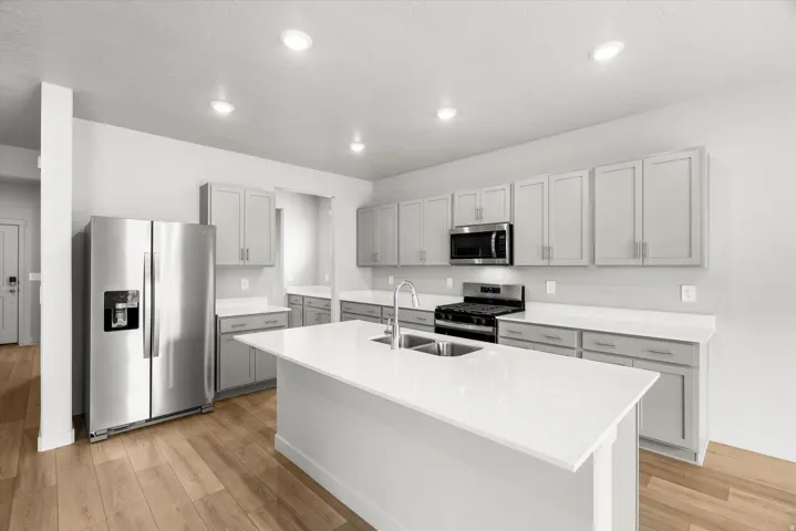 Open-concept kitchen featuring an island with an undermount sink, stainless steel appliances, light gray shaker cabinetry, white countertops, and wood-finish flooring