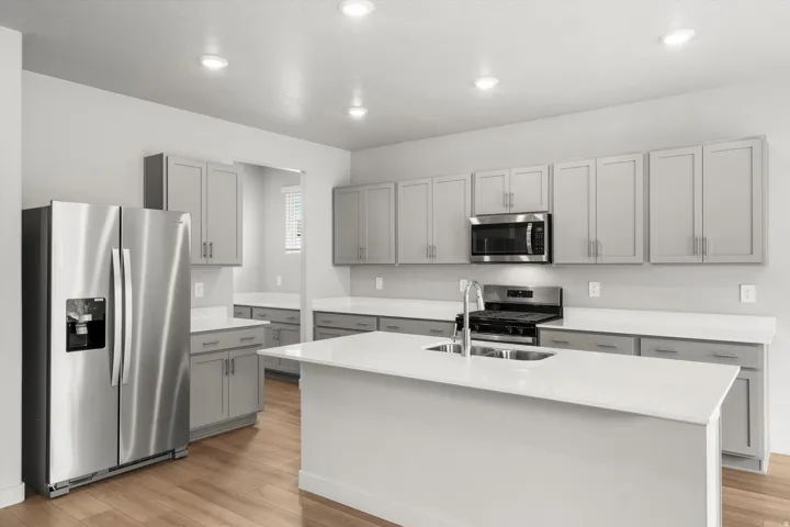 Kitchen featuring light grey cabinetry, stainless steel appliances, a center island with sink, white countertops, and wood-finish flooring