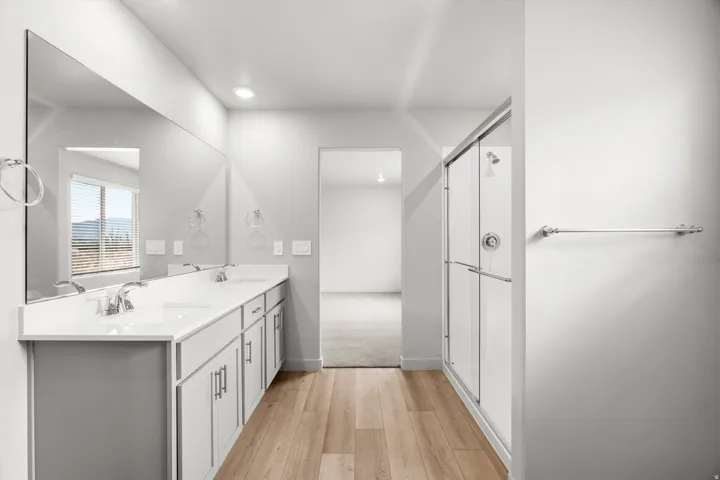 Bathroom featuring a double vanity with white countertops, light wood-finish flooring, a glass-enclosed shower, and a large mirror