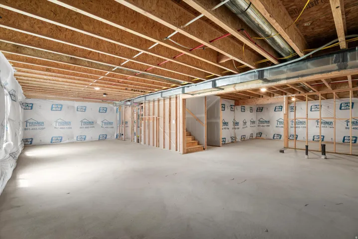 Expansive unfinished basement featuring a concrete floor, exposed wood ceiling joists, framed walls, and a visible staircase