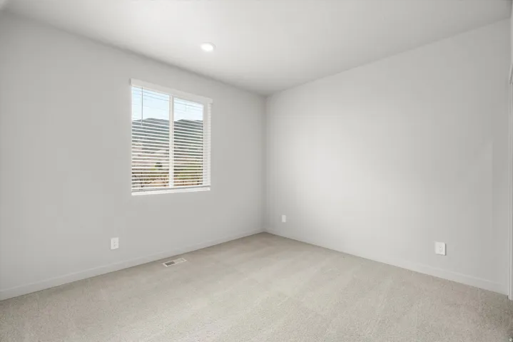 Neutral-toned room featuring a large window with horizontal blinds, carpeted flooring, and recessed ceiling lighting
