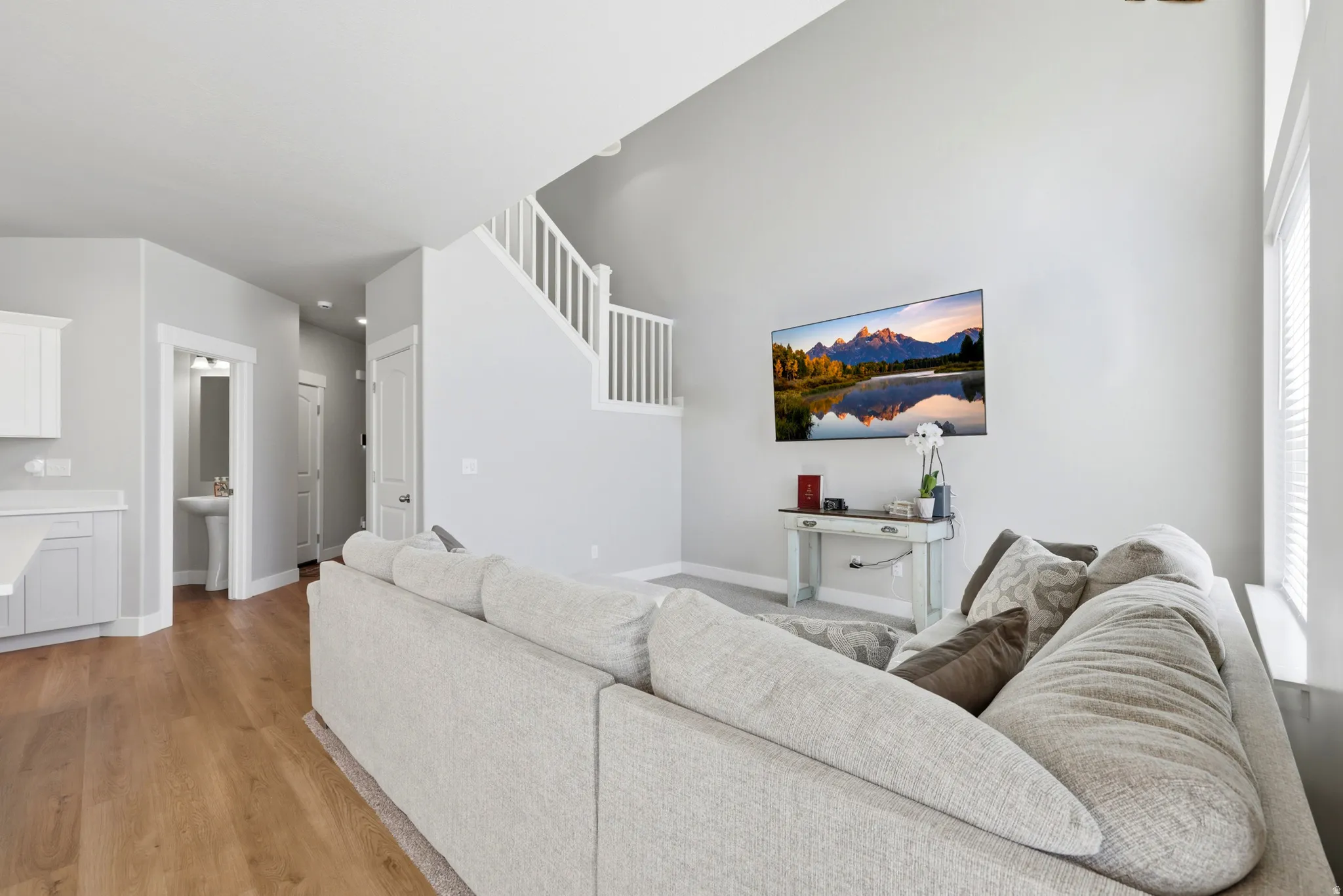 Vaulted living area featuring light wood-finish flooring and a white painted staircase with matching balusters