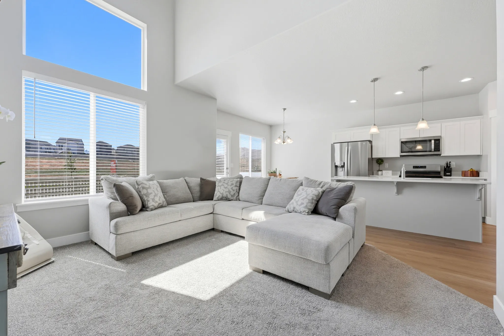Open-concept living space featuring high ceilings, large windows with horizontal blinds, and recessed lighting
