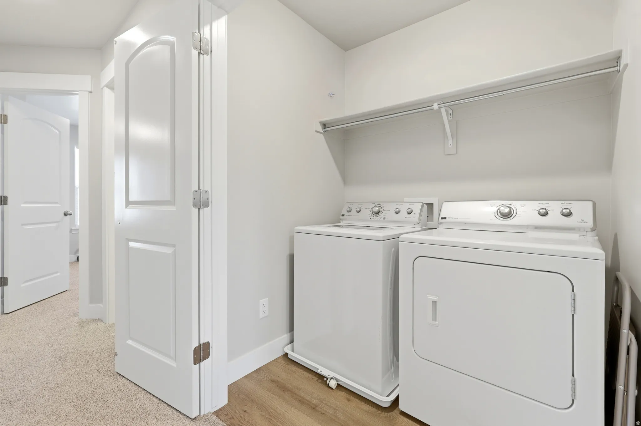 Dedicated laundry area featuring wood-finish flooring, a wall-mounted shelving unit, and white baseboards