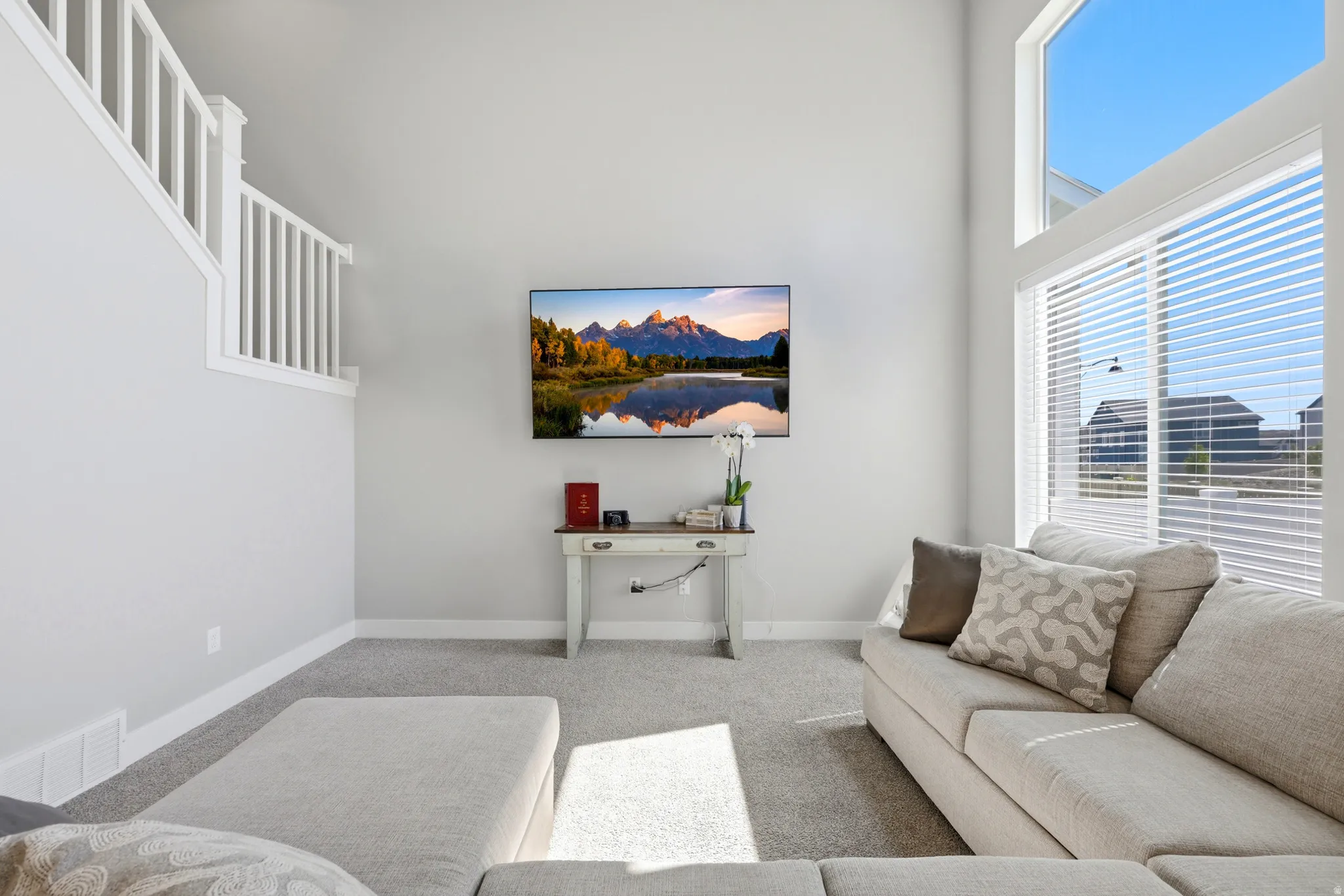 Two-story living area featuring a vaulted ceiling and a large window with horizontal blinds