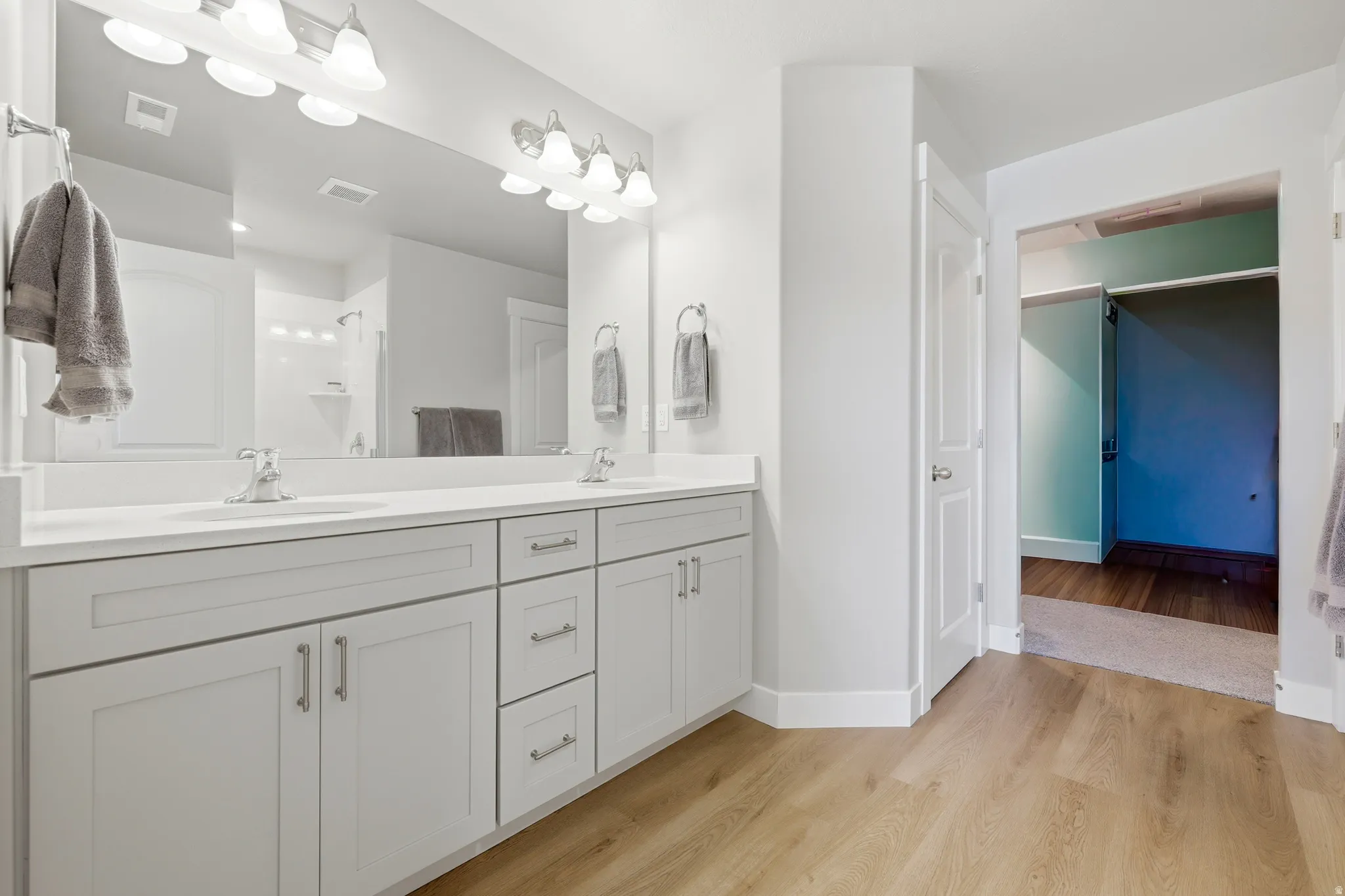 Spacious bathroom featuring a double vanity with light-colored cabinetry, integrated sinks, and polished chrome hardware