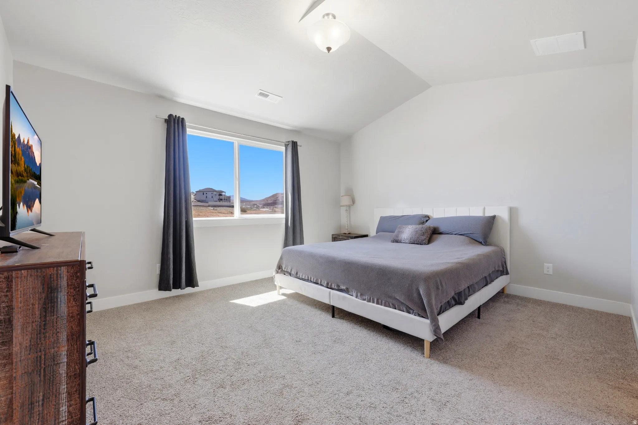Carpeted room featuring a vaulted ceiling and a large window with dark curtains
