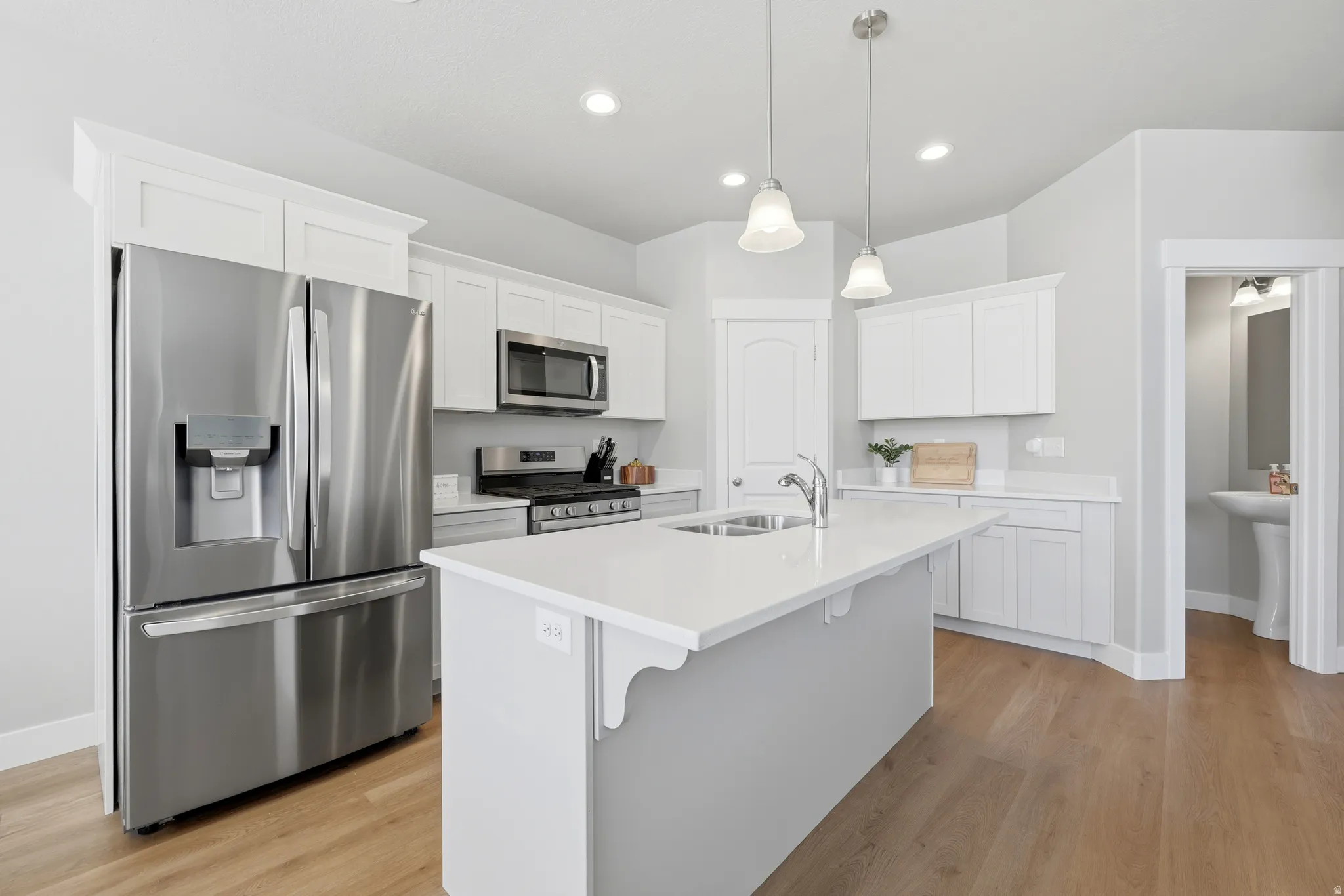Modern kitchen featuring a central island with an undermount sink, white countertops, stainless steel appliances, white cabinetry, and wood-finish flooring