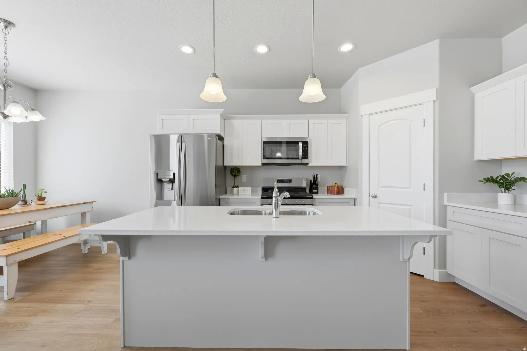 Kitchen featuring a central island with an undermount sink, pendant lighting, white cabinetry, stainless steel appliances, and wood-finish flooring