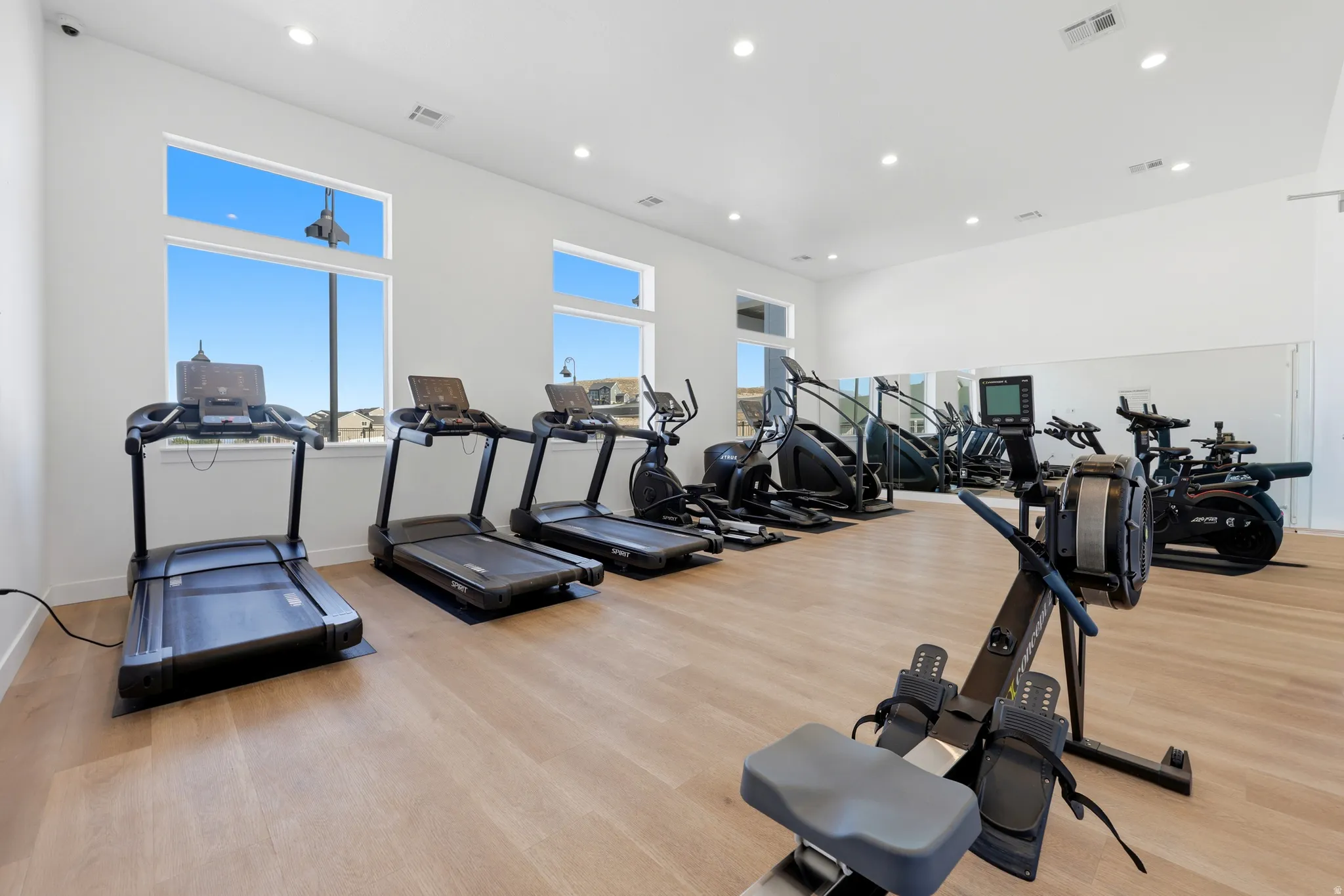 Spacious fitness room featuring light wood-finish flooring, white walls, and recessed lighting