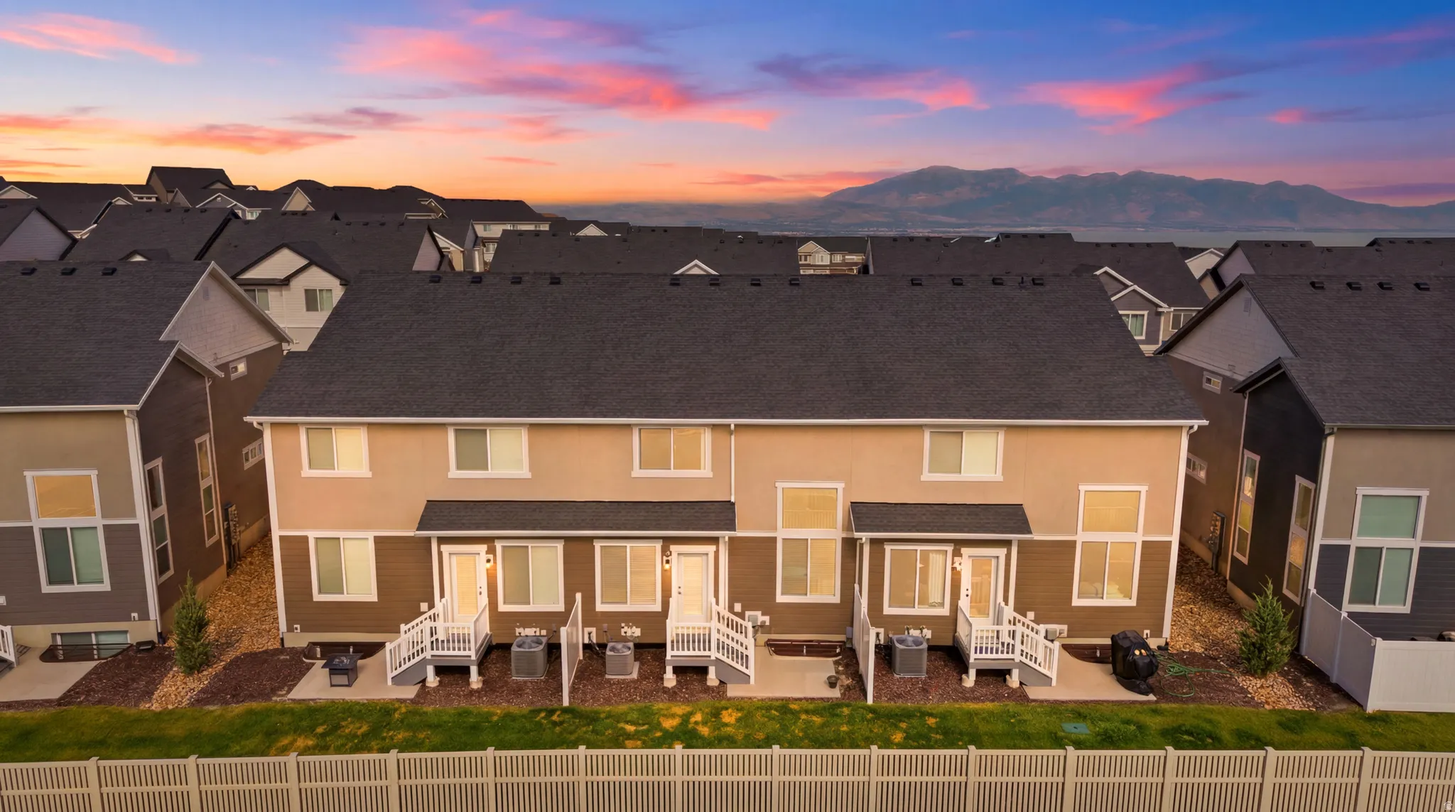 Townhome exterior featuring multi-toned siding, white porch railings, individual patio spaces, and a privacy fence