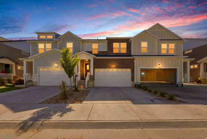 Modern townhome exterior featuring light gray shingle siding, board and batten accents, and brick detailing