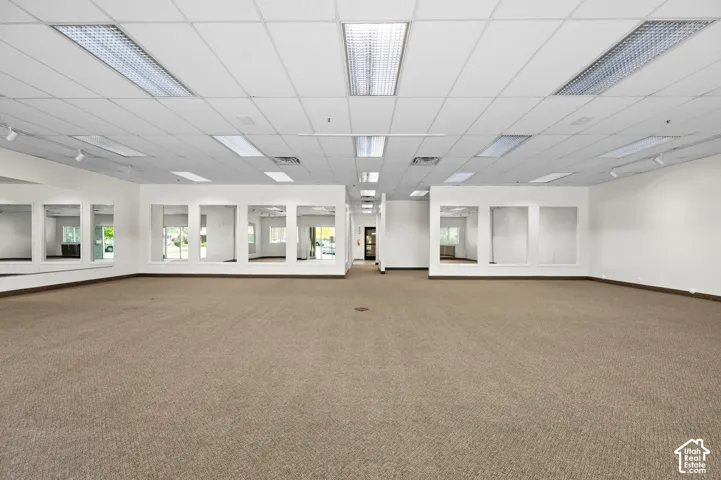 Expansive commercial space featuring neutral carpeting, a dropped ceiling with integrated fluorescent lighting, multiple recessed display niches, and perimeter wall-mounted accent lighting