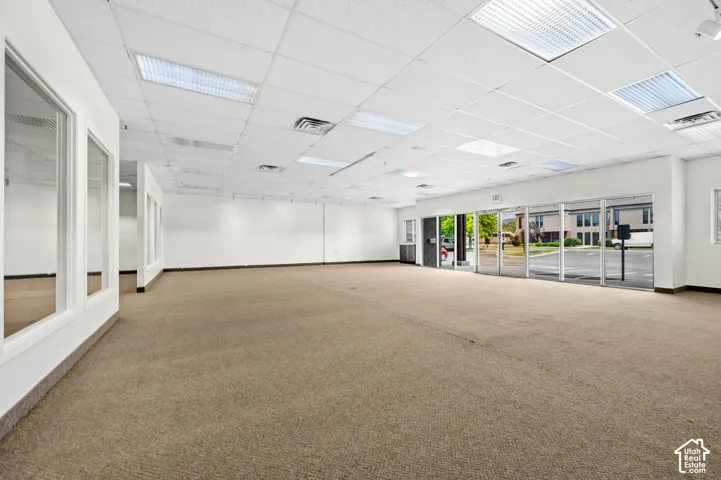 Expansive interior space with commercial-grade carpeting, suspended acoustic ceiling tiles, recessed fluorescent lighting, and extensive window frontage