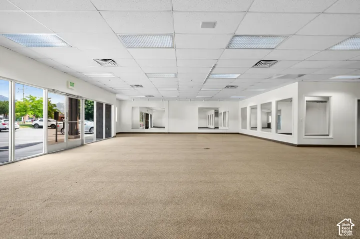 Expansive open-concept commercial space featuring beige carpet flooring and a suspended acoustic ceiling