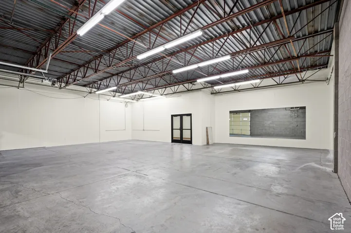Spacious open-concept interior featuring a high exposed truss ceiling, concrete flooring, and fluorescent lighting