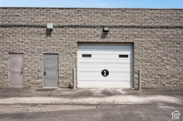 Commercial exterior featuring a white roll-up door with windows, two entry doors, and a textured block facade