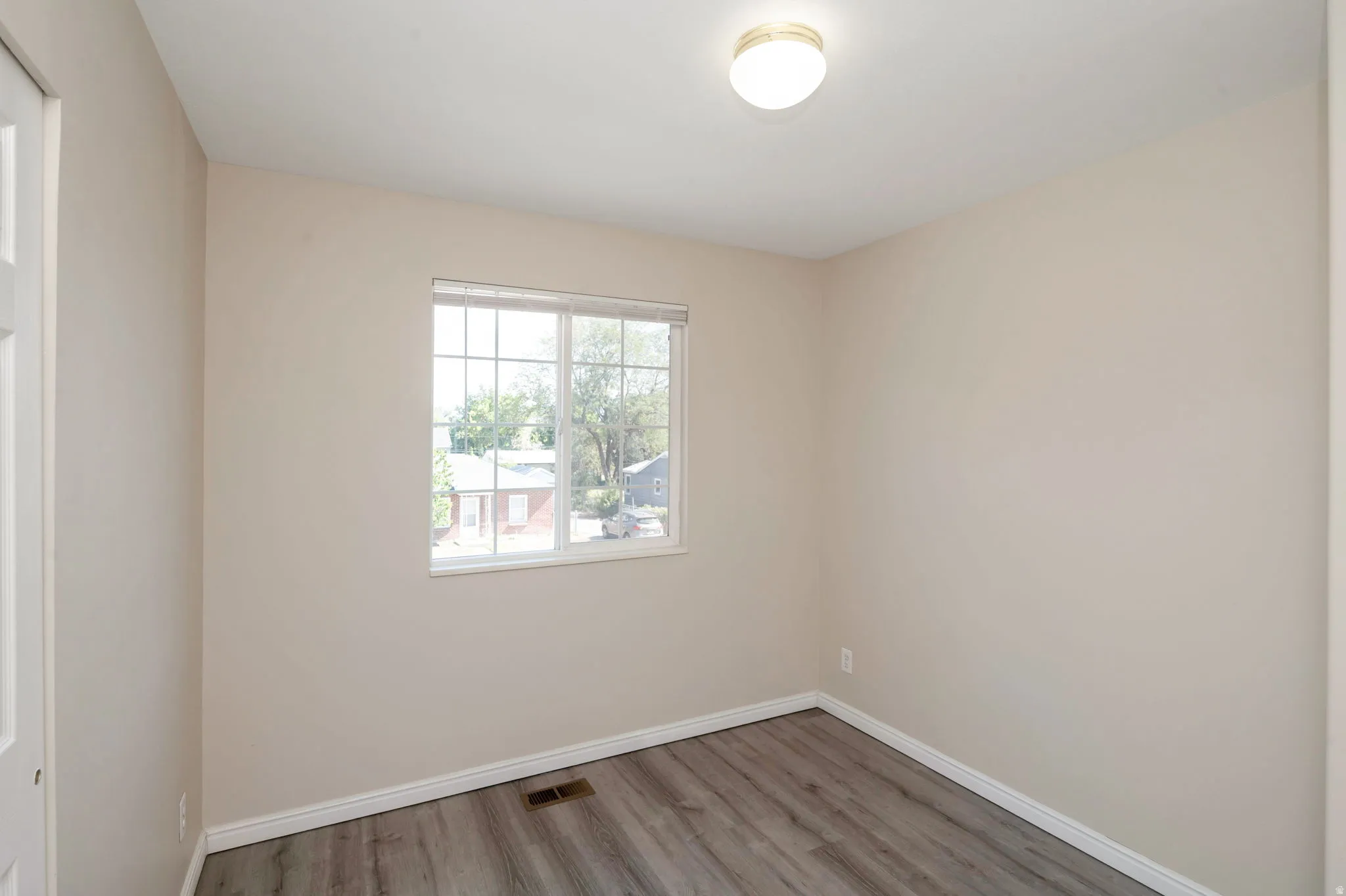 Neutral tone painted walls, wood-finish flooring, white window frame with horizontal blinds, white baseboards, and a flush-mount ceiling light fixture