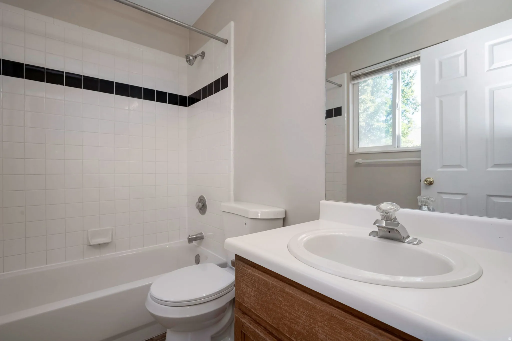 Bathroom vanity with an integrated sink and chrome faucet, set against a white tiled tub surround with a black accent tile band