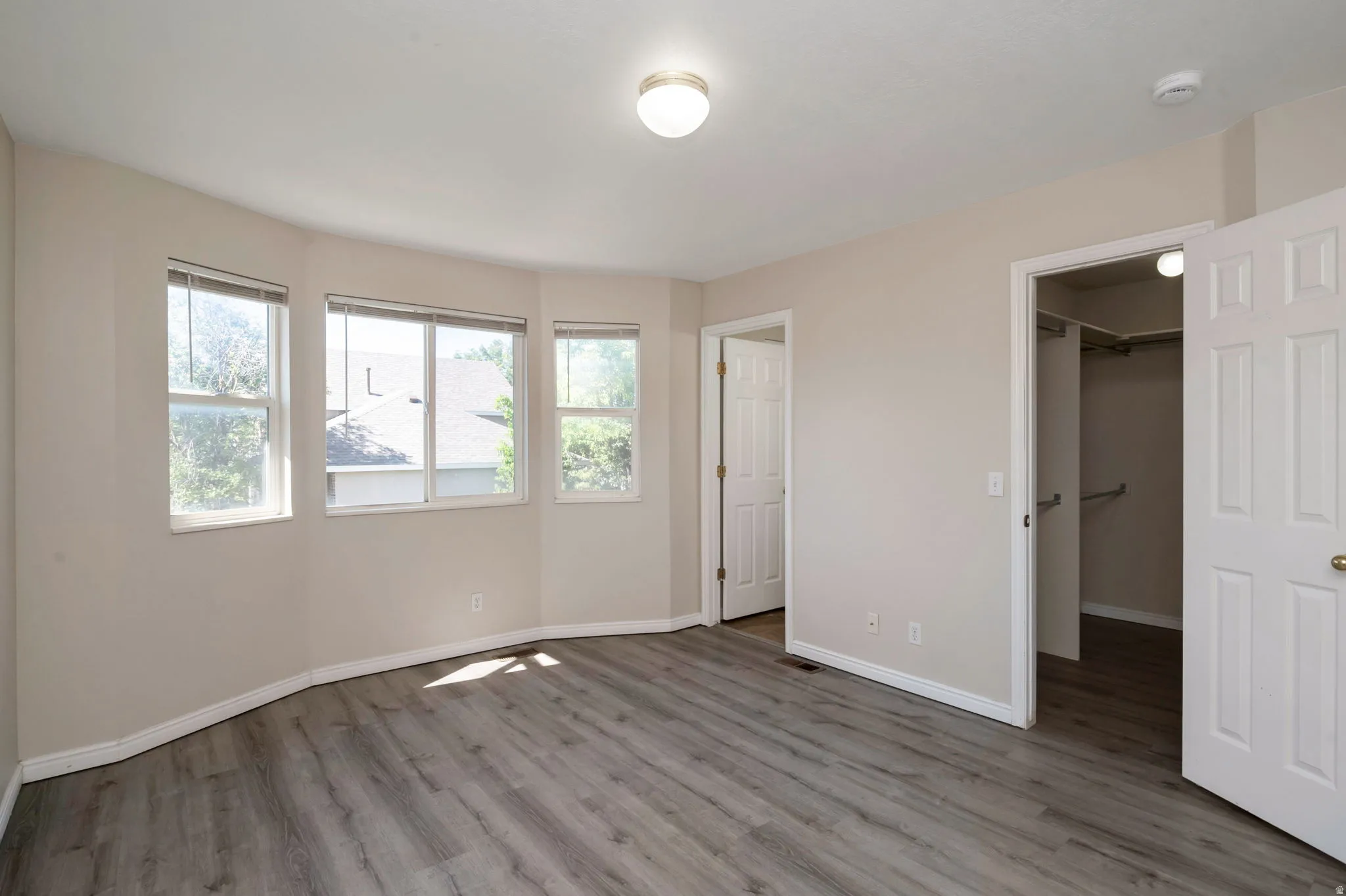 Spacious room featuring multiple windows, wood-finish flooring, light-toned walls, and a built-in closet with hanging rods