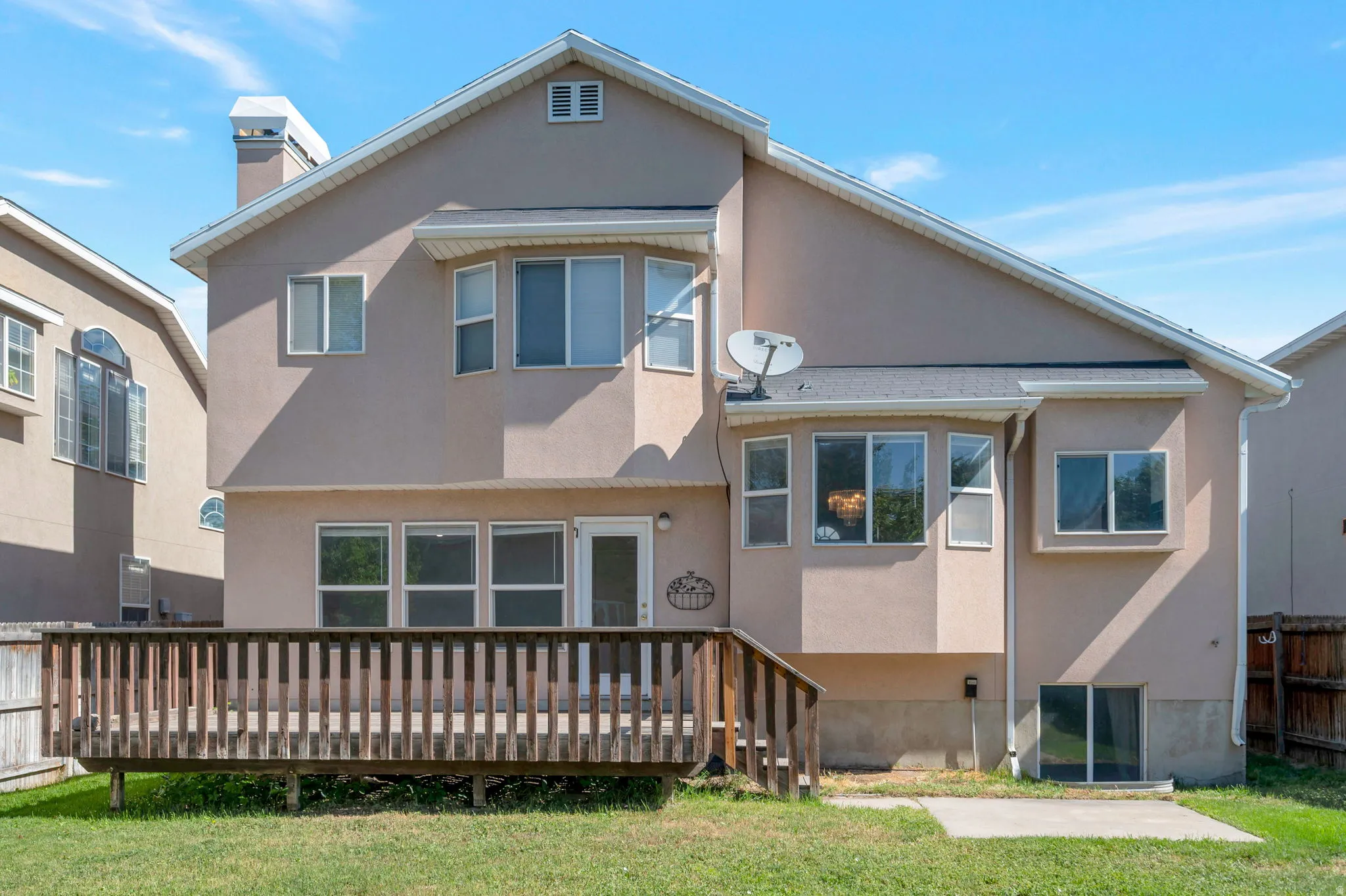 Rear exterior featuring a wooden deck, multiple windows, and a stucco finish