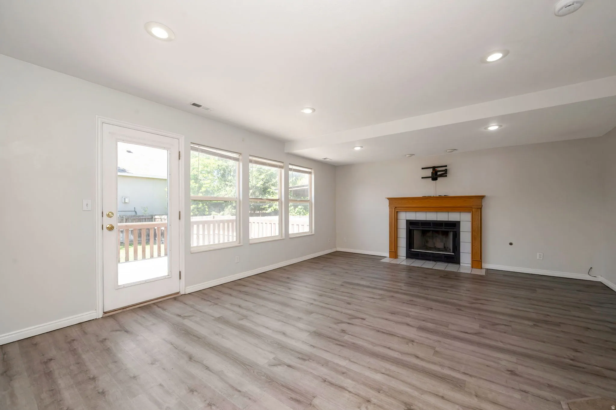Spacious room featuring wood-finish flooring, a fireplace with a wood mantel and tile surround, and recessed lighting
