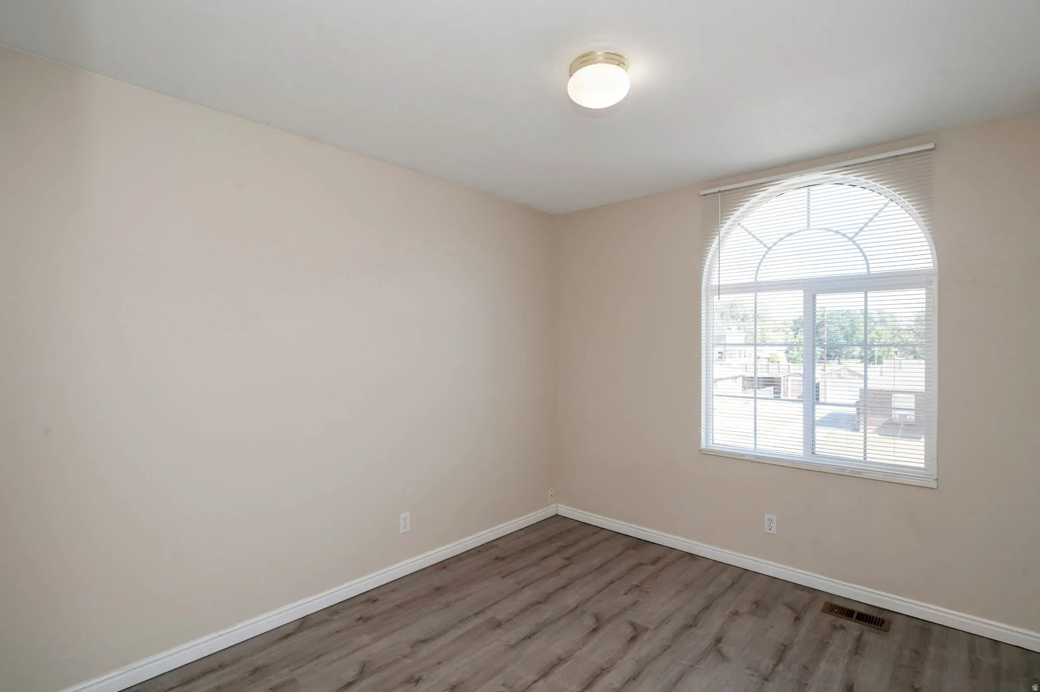 Room featuring a large arched window with blinds, neutral wall paint, and wood-finish flooring