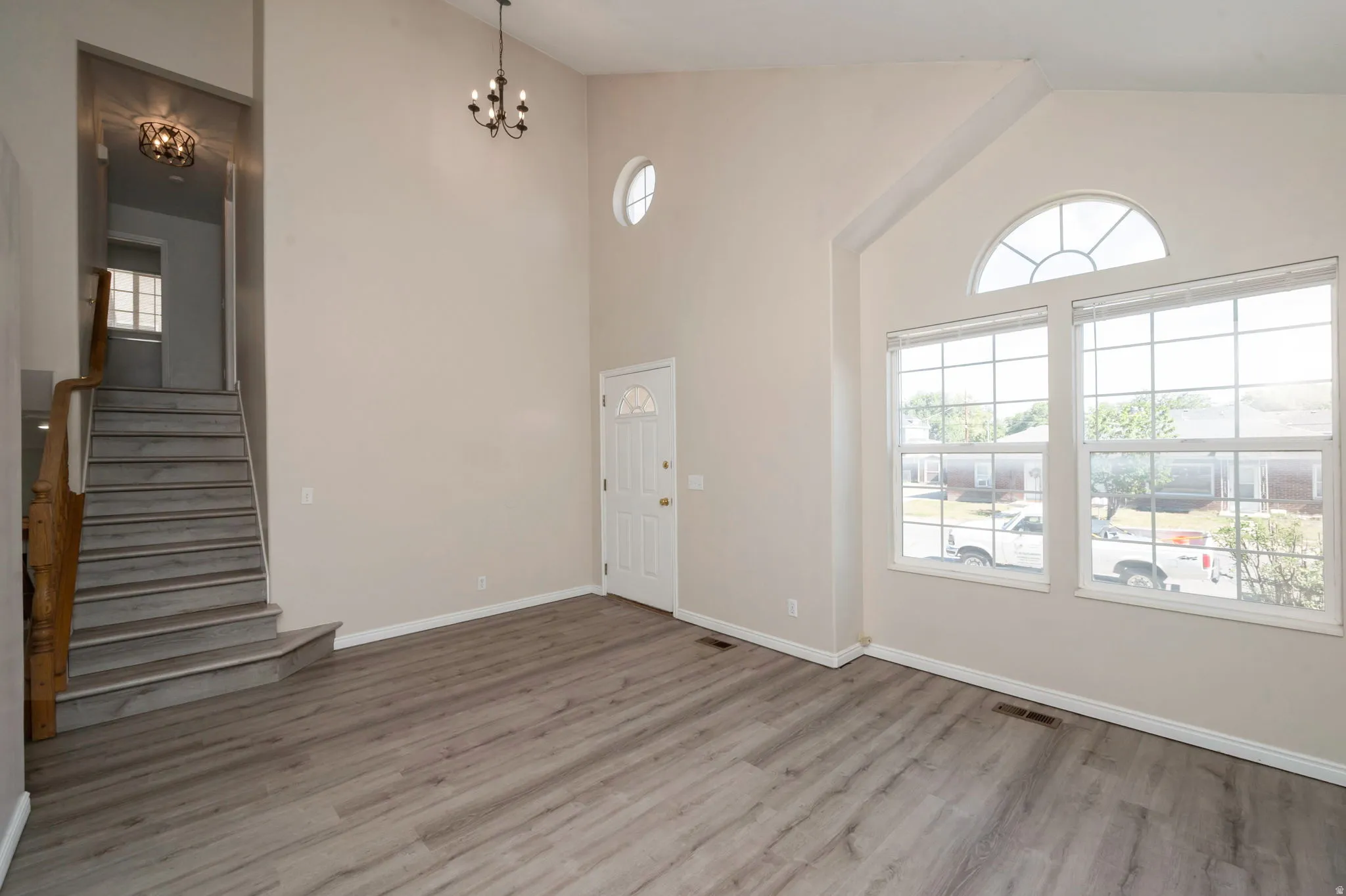 Vaulted living area featuring wood-finish flooring, a decorative chandelier, and an arched window with a transom