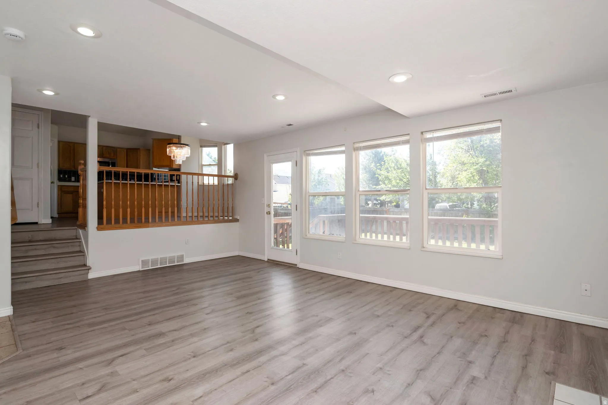 Spacious living area featuring light wood-finish flooring, recessed lighting, and a series of three large windows providing abundant natural illumination