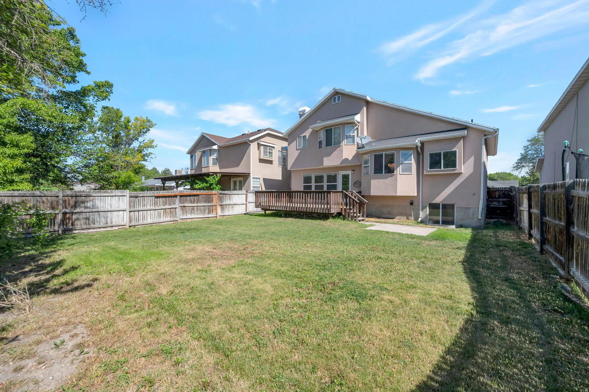 Expansive backyard featuring a wood deck, wood privacy fencing, and a stucco exterior